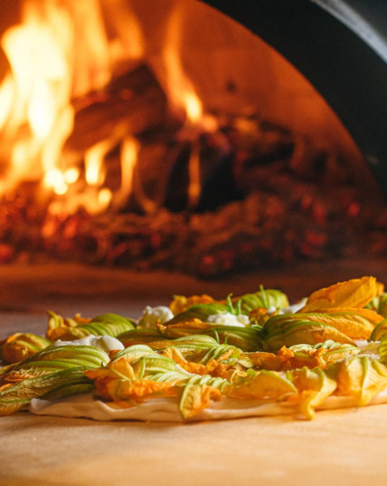 A pizza going into a wood fired oven.