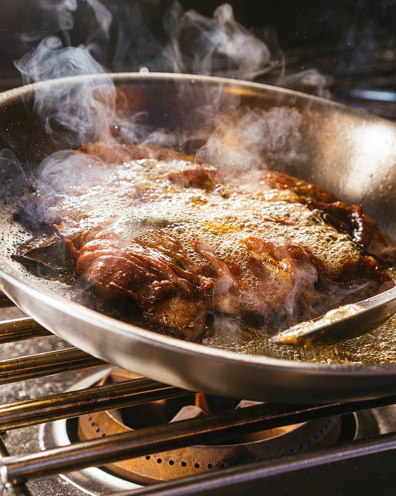 A large slice of meat being cooked in a pan.