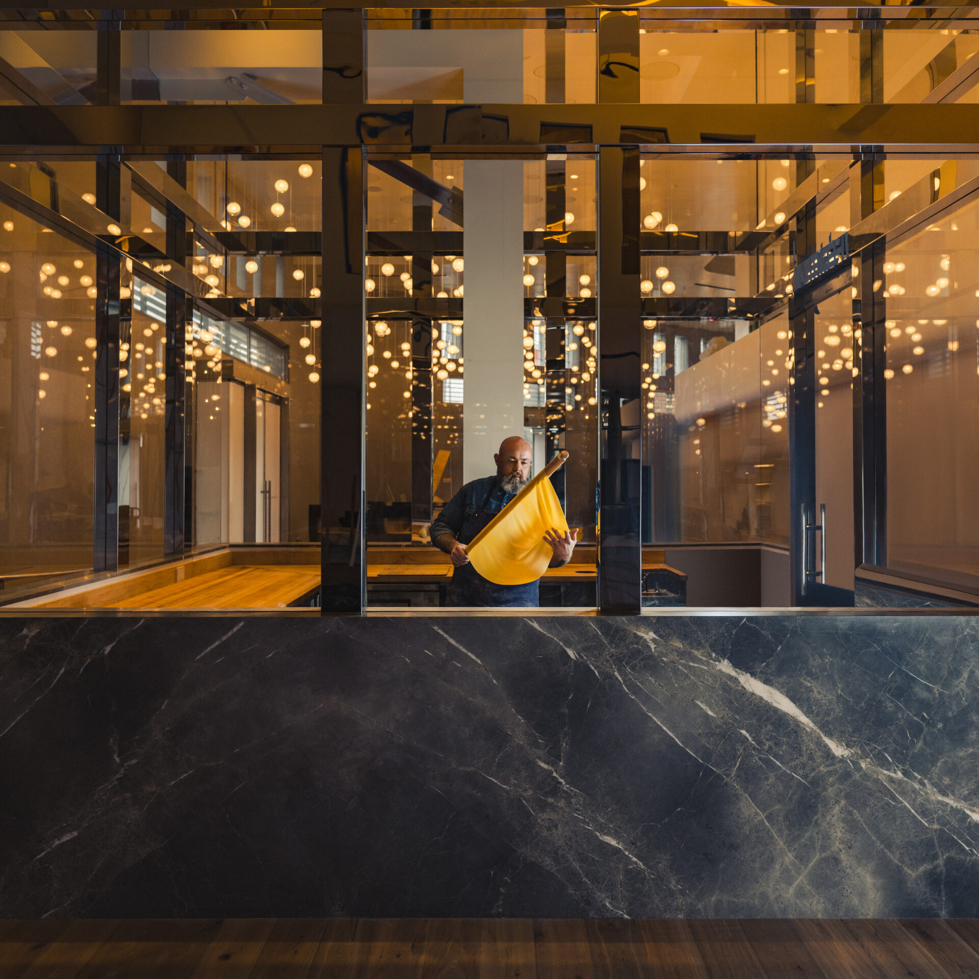 Evan Funke working on pasta in a sleek glass-clad kitchen.